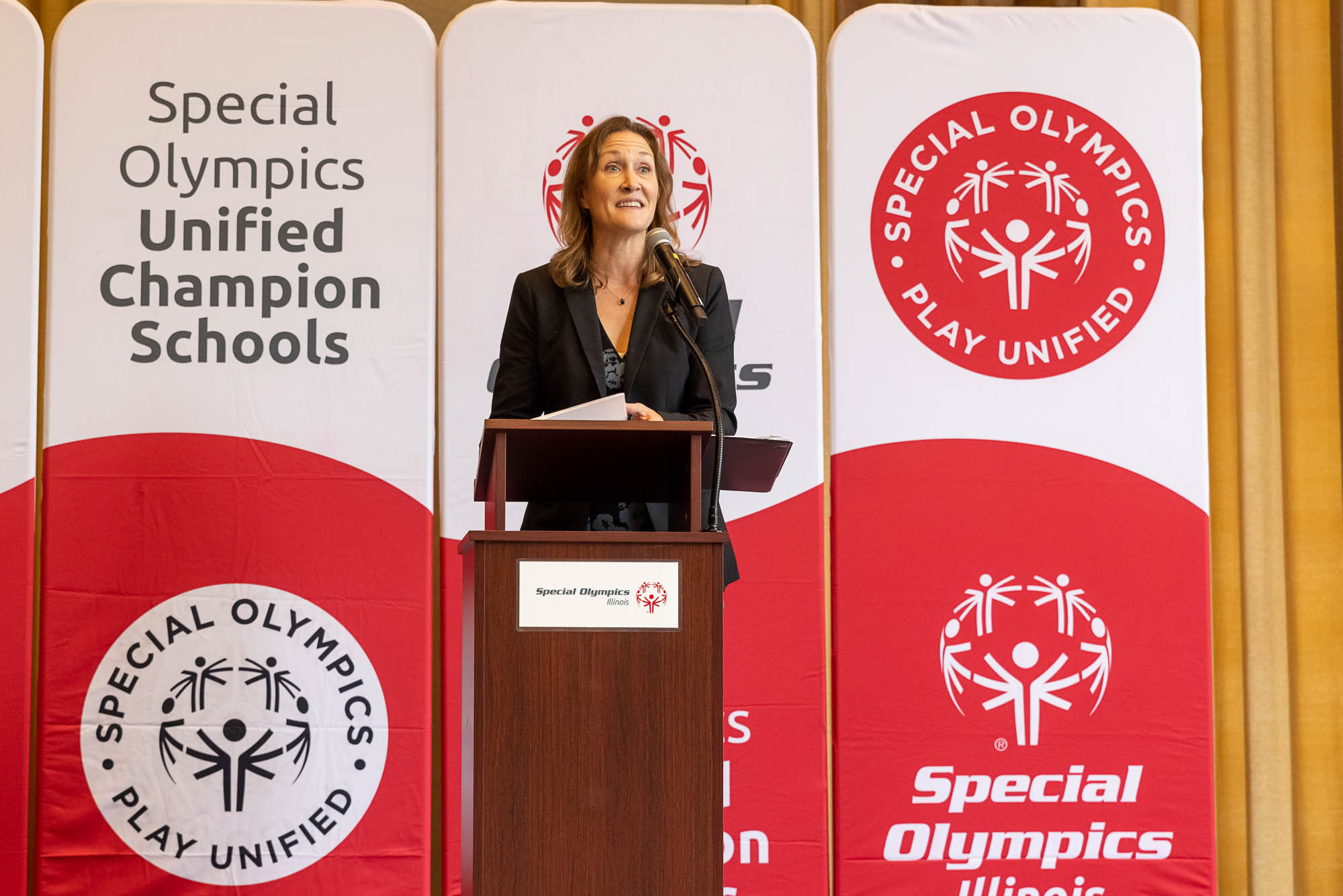 A photo of Rebecca Clark, Anixter's CEO, on a podium in front of a sign that says Special Olympics Unified Champion Schools."