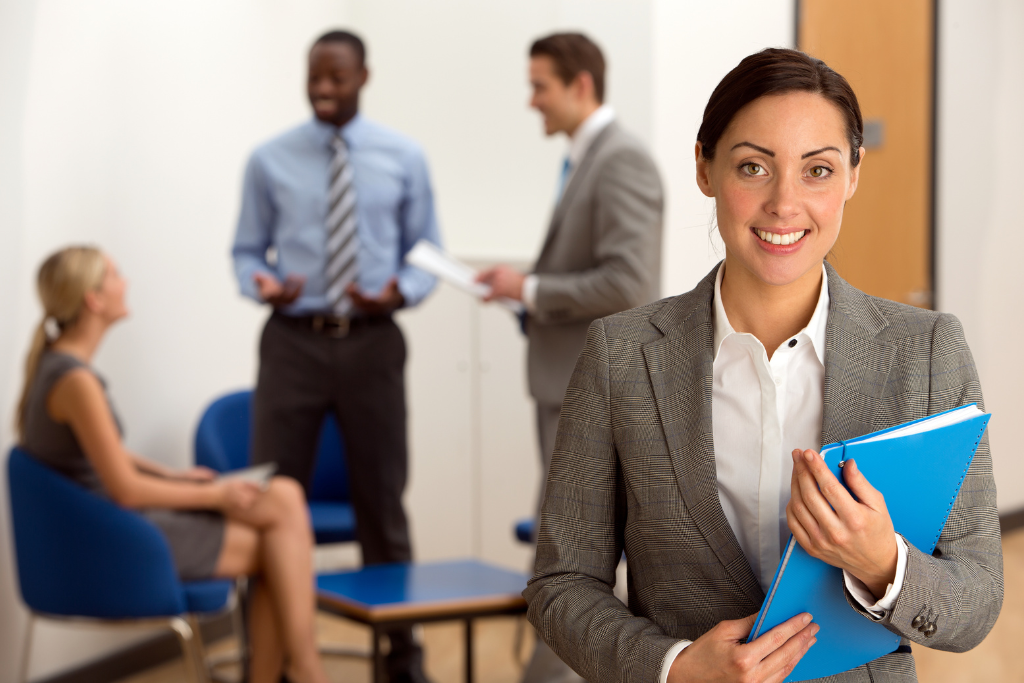 A woman in a business suit smiling with her coworkers in the background.
