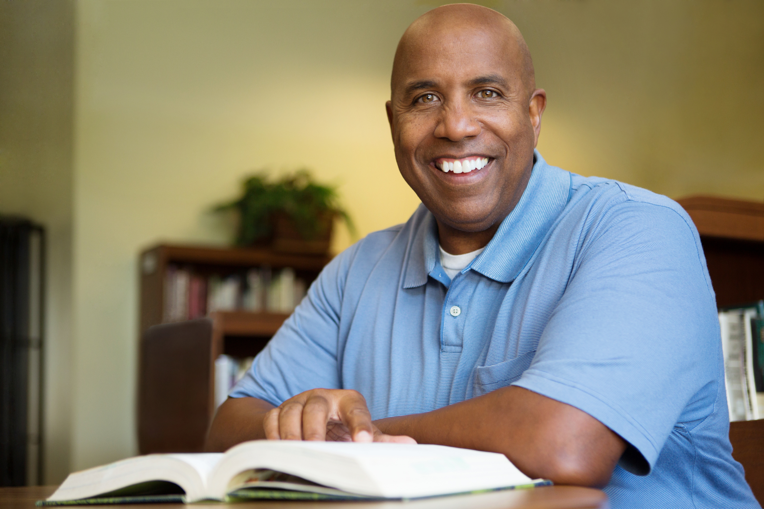 A photo of an adult man reading a book and smiling.